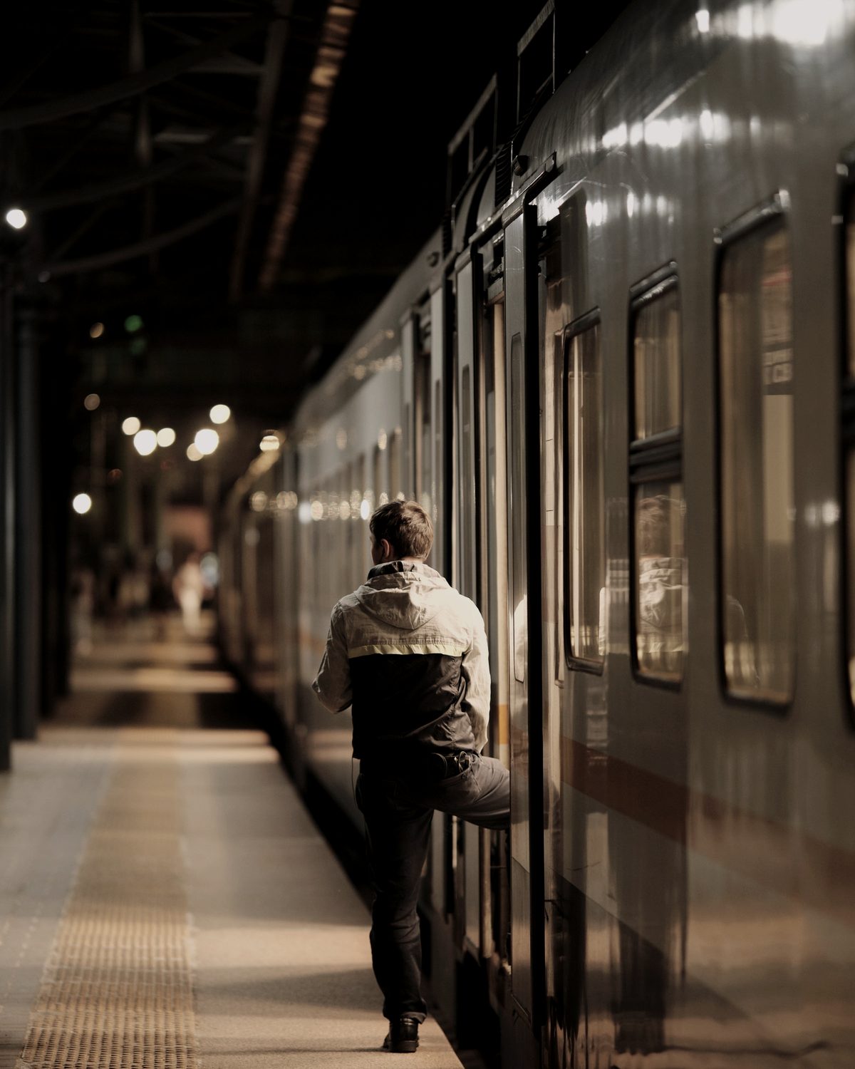 A traveller stepping up into a train door on a night platform, seen from behind.